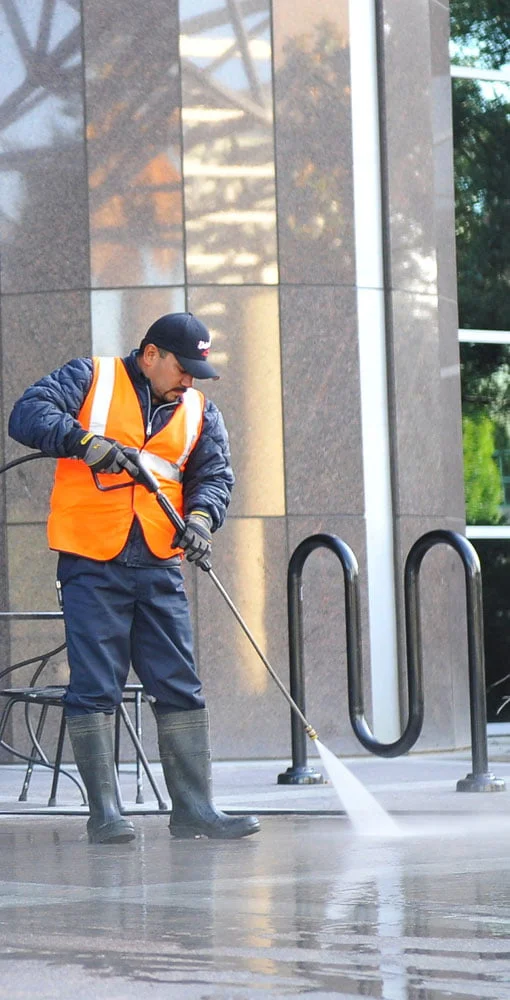 A worker pressure-washing a paved outdoor surface